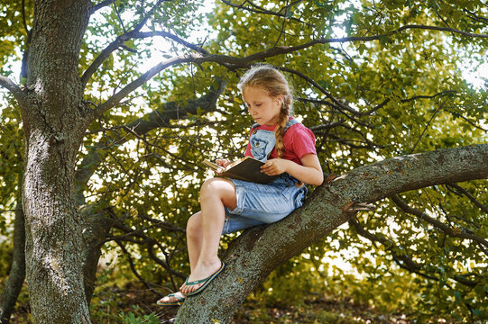 A little girl is reading a book sitting on a tree