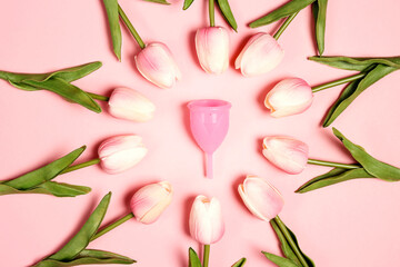 Menstrual cup surrounded by tulips on a pink background.