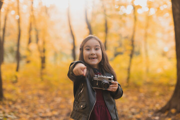 Surprised child girl using an old-fashioned camera in autumn nature. Photographer, fall season and emotions concept.