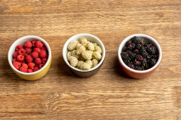 Mix of fresh berries in in bowls on wooden table . Antioxidants, detox diet, organic fruits. Flat lay with copy space.