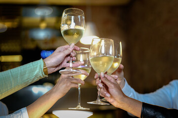 Toast at the restaurant. Detail on the clinkering white wine glasses. Concept of friends having a...