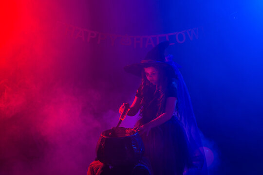 Little witch child cooking potion in the cauldron on Halloween. © satura_