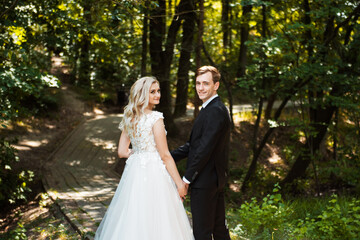 Happy Newlywed woman and man embracing in green park. Loving wedding couple outdoor. Bride and groom. Bride and groom at wedding day walking outdoors on summer green nature