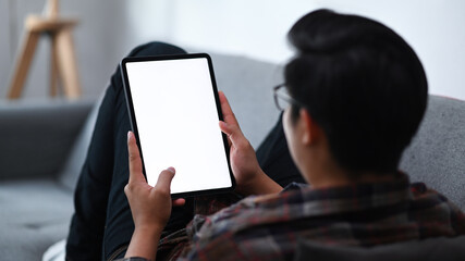 Back view casual man sitting on couch and using digital tablet.
