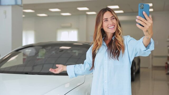 Fun adult woman customer female buyer businesswoman client wear classic shirt doing selfie shot on mobile cell phone in car showroom vehicle salon dealership store motor show indoor. Car sales concept