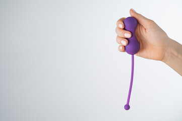 A faceless woman holding an electronic Kegel trainer for training pelvic floor muscles on a white...