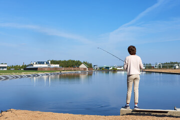 Naklejka premium angler woman in light clothes is catching spinning fish in pond on the summer sunny day