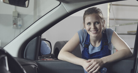 Smiling female mechanic leaning on a car window