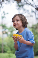 Portrait of adorable little boy eating corn in park. Cute toddler enjoying fresh vegetable. Childhood, healthy eating, fresh food concept