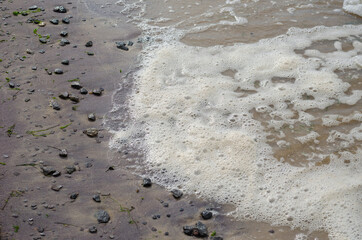 Sandy beach after the storm at sunset. Muddy Shoreline with pebbles and algae. August, evening time. Angled view from above. Selective focus. Blurred motion.