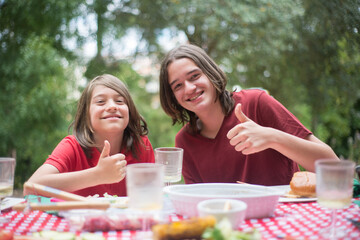 Happy children eating together. Two schoolboys enjoying food. Showing thumbs up. Family time, outdoor activity, picnic concept