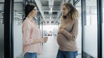 Friendly employee talking to pregnant colleague in office, maternity leave