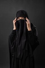 Portrait of a young, adult woman in a black burqa with a hidden face isolated on a black background.