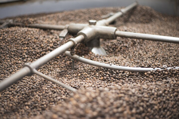 Close-up of roasted coffee beans in roasting machine. Interior of coffee production workshop with...