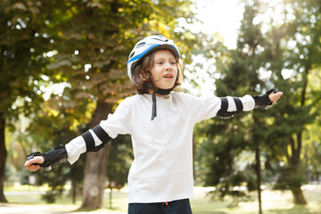 Happy young boy wearing helmet and skate pads, enjoying rollerblading at the park © Ihor
