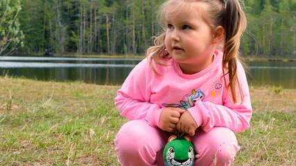 Portrait of funny 3 year old girl, dressed in a pink sweatshirt with two ponytails, playing outdoors in nature. Happy childhood concept, children development