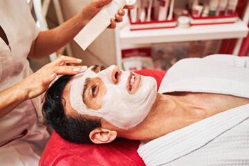 Obraz na płótnie Canvas Beautician putting facial cream mask on man face