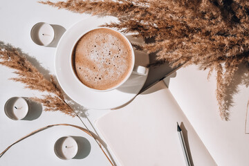 Pampas grass and white cup with coffee. Empty notebook making a plan for the day. Drinking Cappuccino in the breakfast morning at home. Flat lay. Wallpaper. Aesthetics