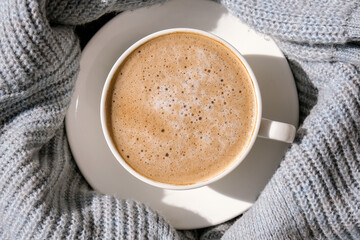 White cup of morning coffee on blue sweater background. Cozy home autumn concept. Aesthetics blog lifestyle. Still life concept. Cappuccino or latte hot drink