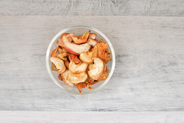 A pile of dried apples in slices on a white plate on wooden background. Top view with copyspace