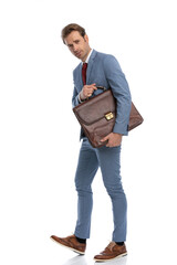side view of attractive young man in blue suit holding suitcase