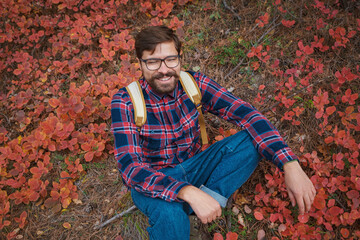 Male hipster Traveler with backpack in plaid shirt and jeans hiking in the mountains travel, trekking in autumn countryside. beautiful red leaves on the slopes