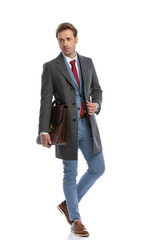 cool elegant fashion man with suitcase fixing coat and looking to side