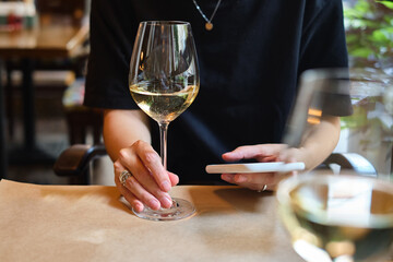 A glass of white wine in the hands of a girl relaxing in a restaurant. Tasting of alcoholic beverages. Summer rest. Romantic evening aperitif. Close-up of a glass of wine. Enjoy the moment