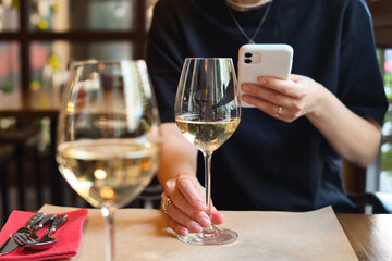 A glass of white wine in the hands of a girl relaxing in a restaurant. Tasting of alcoholic beverages. Summer rest. Romantic evening aperitif. Close-up of a glass of wine. Enjoy the moment