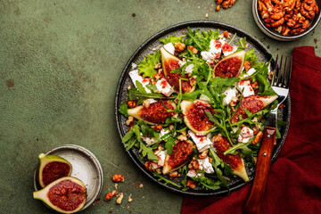 Fig salad with white cheese, walnuts, arugula and jam dressing on rust green background, top view, copy space
