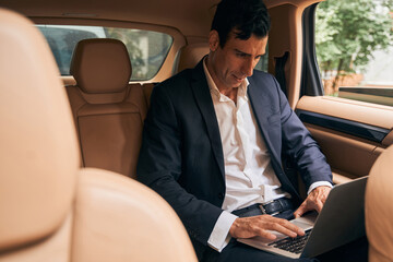 Focused businessperson typing on laptop keyboard from car