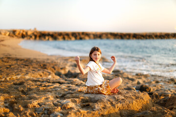 Fototapeta na wymiar Cute caucasian child girl with long hair meditates by the sea, silence and calmness, warm toning