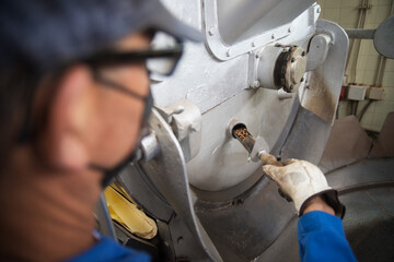 Man checking quality of roasted coffee. Coffee roaster working on roasting equipment. Man in mask and uniform Working with machinery appliance. Coffee in special scoop. Production, food concept