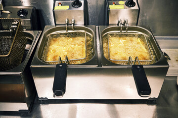 French fries potatoes frying in the hot fryer of a restaurant kitchen. 