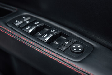 Close-up of the side door buttons: window adjustment buttons, door lock. Mirror control knob and window control panel in a modern car. Automatic car window controls and details. Selective focus.