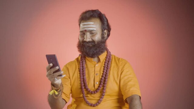 holy Indian Monk or guruji receiving phone call and giving suggestions or telling fortune to his devotees - concept of Hinduism, superstition and communication