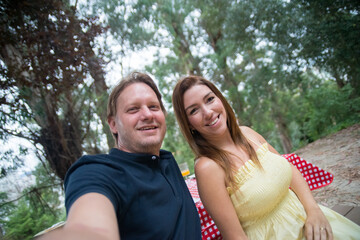 Happy husband and wife taking selfie. Smiling mid adult man and woman sitting together, smiling at mobile phone, taking pictures. Family time, outdoor activity, social media concept