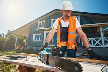 Worker in safety vest grabbing chainsaw from table