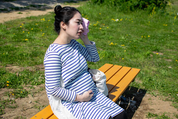A young pregnant Asian woman sitting on the outside bench and wiping sweat way
