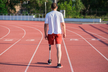 Fototapeta premium Caucasian male athlete with a prosthesis on his leg walking on the track at the stadium. Back view. Sport concept.