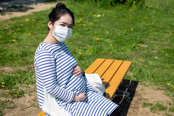 Fototapeta premium A young pregnant Asian woman sits on the outside bench and worries about her baby in her stomach