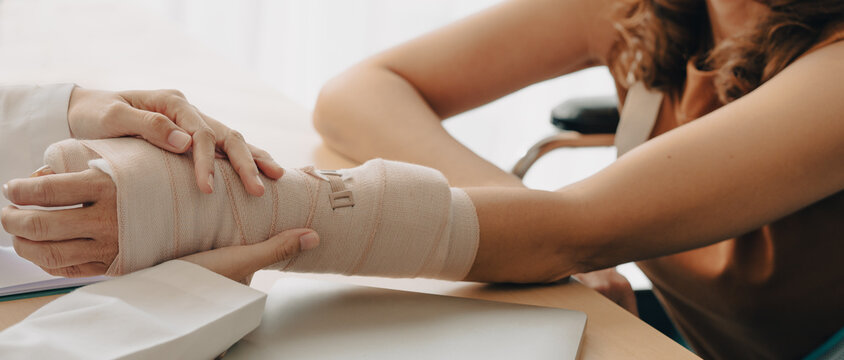 Close up of orthopedic doctor investigates woman patient broken arm covers with a splint plaster cast. Trauma can happen after people fall and are hurt physically by accidents. Rehab center services.