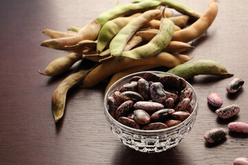 Scarlet runner bean in a small crystal glass bowl on a dark surface with green and yellow hulls in a background.