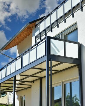 Moderner Balkon mit Sichtschutz aus Mattglasplatten und Metall-Geländer an einer Neubau-Hausfront