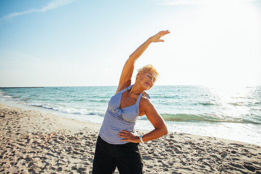 Active senior woman stretching by the sea at sunrise