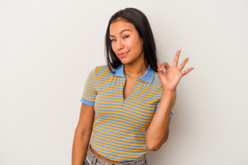 Young latin woman isolated on white background  winks an eye and holds an okay gesture with hand.