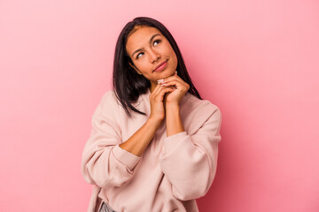 Young latin woman isolated on pink background  keeps hands under chin, is looking happily aside.