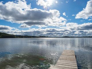 Wooden pier on the shore of the lake. Clouds in the sky on a sunny day.