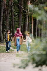 Fototapeta premium Cheerful arabian mother in hijab walking with kids in park