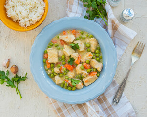 Chicken stew or indian curry with carrots and green peas in a gray plate on a light concrete background. Served with rice.